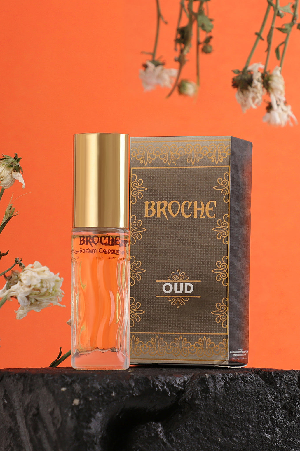 broche-oud-perfume-15ml-with-bottle-and-packaging-on-rock-with-orange-background-and-flowers